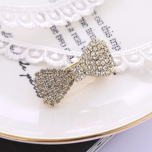 Elegant gold bow hair clip with sparkling rhinestones on white lace and ceramic tray