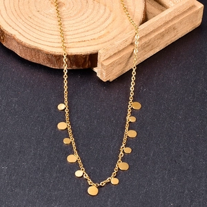 Detail of a dainty gold necklace with small circular disks on rustic wooden decor