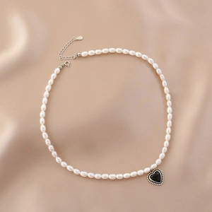 Detail of freshwater pearl necklace with black heart pendant on silk background