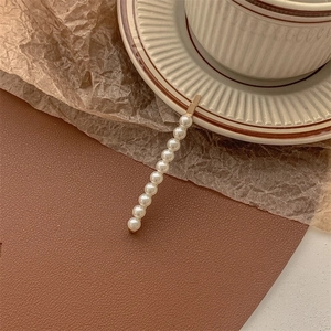 Detail of elegant gold alloy hair clip featuring 11 white round pearls on a textured background
