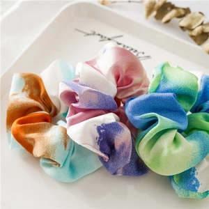 Three tie-dye elastic scrunchies in vibrant gradients on a white decorative tray