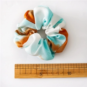 Tie-dye satin scrunchie with blue and orange abstract pattern and a size reference ruler