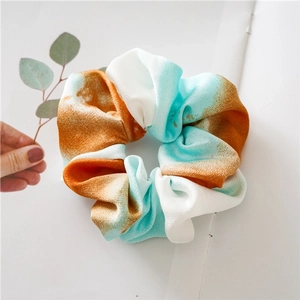 Macro detail of a colorful tie-dye scrunchie in orange, white and teal chiffon fabric