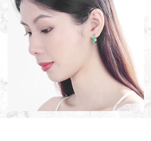 Detail showing the green rectangular earring with silver edges worn by a model on a white ear