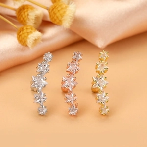 Close-up of star shaped cartilage earrings with zircon stones in silver, gold and rose gold