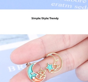 Detail of gold star and crescent moon earrings with colorful enamel and eyelash accents