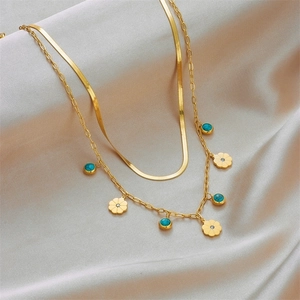 Double-layered gold snake chain necklace with turquoise flower pendant on silk background
