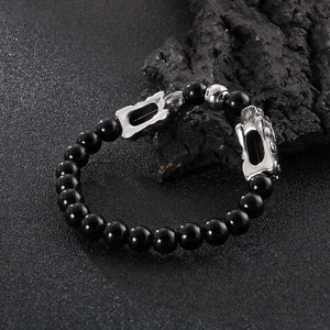 Handmade black beaded bracelet with silver Pi Xiu charms on dark stone surface
