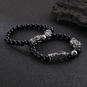 Beaded Pixiu bracelet with black obsidian stones and silver-toned metal charms on wood