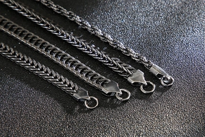 Macro view of four braided wheat chain necklaces in dark grey stainless steel finish