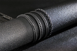Detailed view of black stainless steel woven chain bracelet on dark textured display