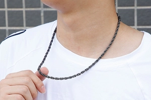 Close-up of a dark grey stainless steel braided rope chain necklace worn by a male model