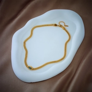 Minimalist gold chain necklace with a blue evil eye pendant on a white ceramic tray