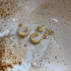 Macro shot of 925 silver gear earrings and gold chain jewelry on a rustic ceramic plate