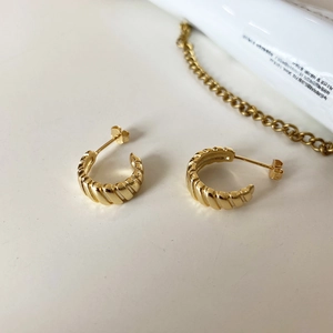 Close-up of golden ribbed croissant earrings with high polish on minimalist white surface