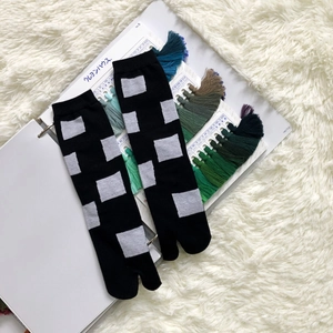 Detail of black tabi split-toe socks with grey geometric jacquard on soft plush rug
