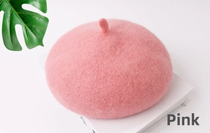 Dettaglio di un basco in lana rosa per bambini esposto su un libro decorativo bianco