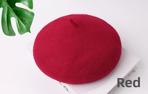 Dettaglio della trama del basco in feltro di lana rosso vino su un libro bianco con foglia