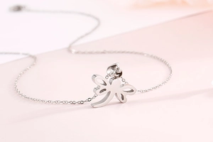 Macro detail of silver dragonfly pendant on fine O-chain over soft pink surface