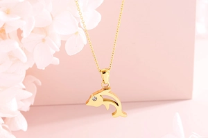 Detailed close-up of golden dolphin pendant with clear gemstone eye on a floral background