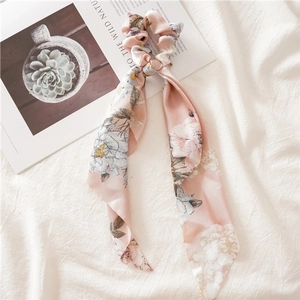 Detail view of pink floral hair scrunchie with long ribbons on a minimalist fabric background