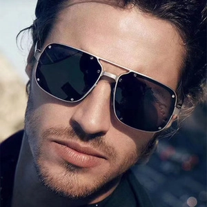 Detail of silver metal square sunglasses with rivets worn by a male model outdoors