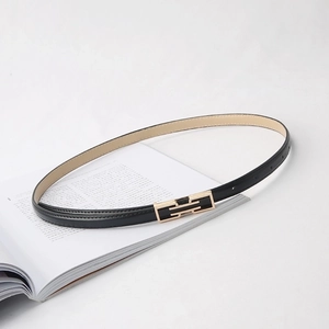 Slim black faux leather belt with a rectangular gold buckle on a minimalist book background