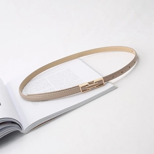 Detail of a thin beige leather belt with a golden metal buckle on a white background