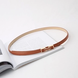 Close-up of a slim brown leather belt with a gold geometric buckle on a magazine