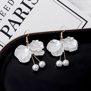 Close-up of white petal earrings with pearls and gold metal hooks on a black plate