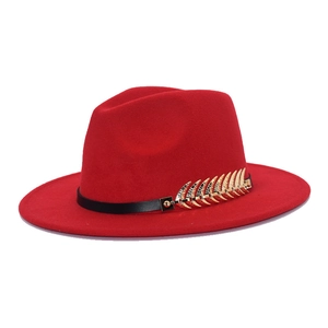 Close-up of a red fedora hat with a black textured band and gold leaf metal accessory