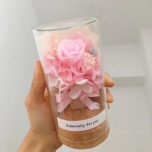 Mini glass dome with pink rose and dried flowers on a cork base, held in hand