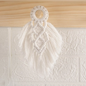Detail of white cotton macrame feather wall hanging on a rustic wooden hook