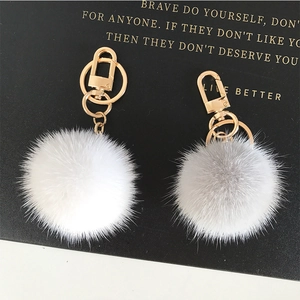 Detail of white and light grey fluffy fur pompom keychains with gold lobster clasps