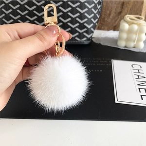 Close-up of fluffy white fur pompom keychain with a golden metal ring on a handbag