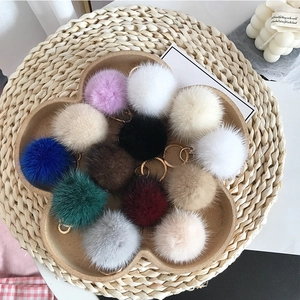 Colorful mink fur puff keychains with gold rings displayed on a wooden tray