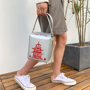 Silver cube handbag with red pagoda print and gold chain strap held by a model