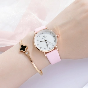 Detailed shot of a pink leather watch and a gold clover bracelet on a woman's wrist