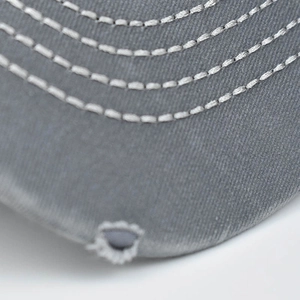 Macro shot of gray washed cotton baseball cap brim with white stitching and distressed holes