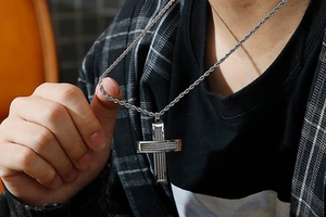 Close-up of a silver cross pendant with steel wire texture on a braided chain