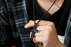 Close-up of hip-hop men's black wire cross necklace worn over a checkered shirt