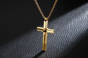 Macro shot of gold cross pendant on rope chain against a black textured leather background