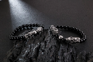 Detailed close-up of obsidian beaded bracelets with silver Pixiu charms on dark rock