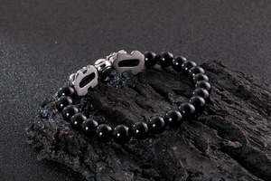 Close-up of black obsidian beaded bracelet with silver Pi Xiu charms on volcanic stone