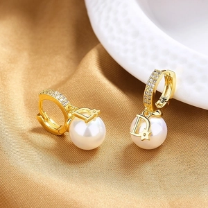 Vintage gold D-letter earrings with white pearl and star accents on silk background