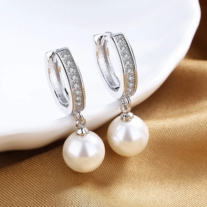 Macro detail of silver U-shaped pearl earrings with cubic zirconia on white porcelain