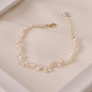 Detail of baroque pearl bracelet with gold lobster clasp on beige textured fabric