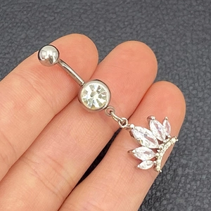 Macro detail of silver navel ring with crown pendant and marquise-cut zircon stones