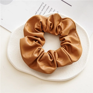 Detailed texture of brown PU leather scrunchie on a decorative white plaster tray