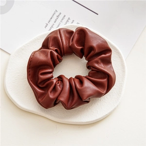 Detailed texture of a brown PU leather scrunchie placed on a white gypsum tray